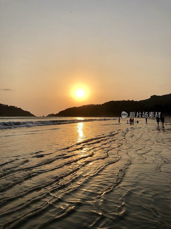 美丽的海边橙色日落日出反射在大海和潮湿的沙子在帕洛伦海滩，果阿/喀拉拉邦，印度，温柔的海浪，潮水反射涟漪，游客步行海岸在冬季假期，热带岛屿上的太阳日落